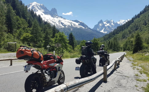 Image of motorbikes parked on the side of a mountain road in the Pyrenees with snow-capped mountains in the distance
