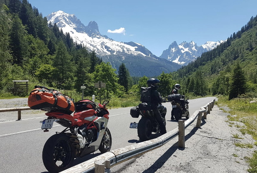 Image of motorbikes parked on the side of a mountain road in the Pyrenees with snow-capped mountains in the distance